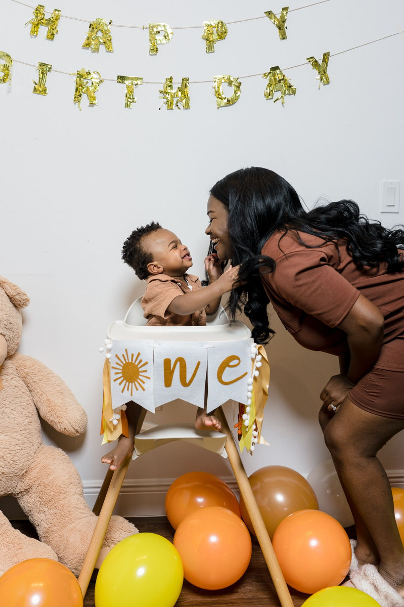 Woman leaning toward a baby in a high chair beneath a Happy Birthday banner