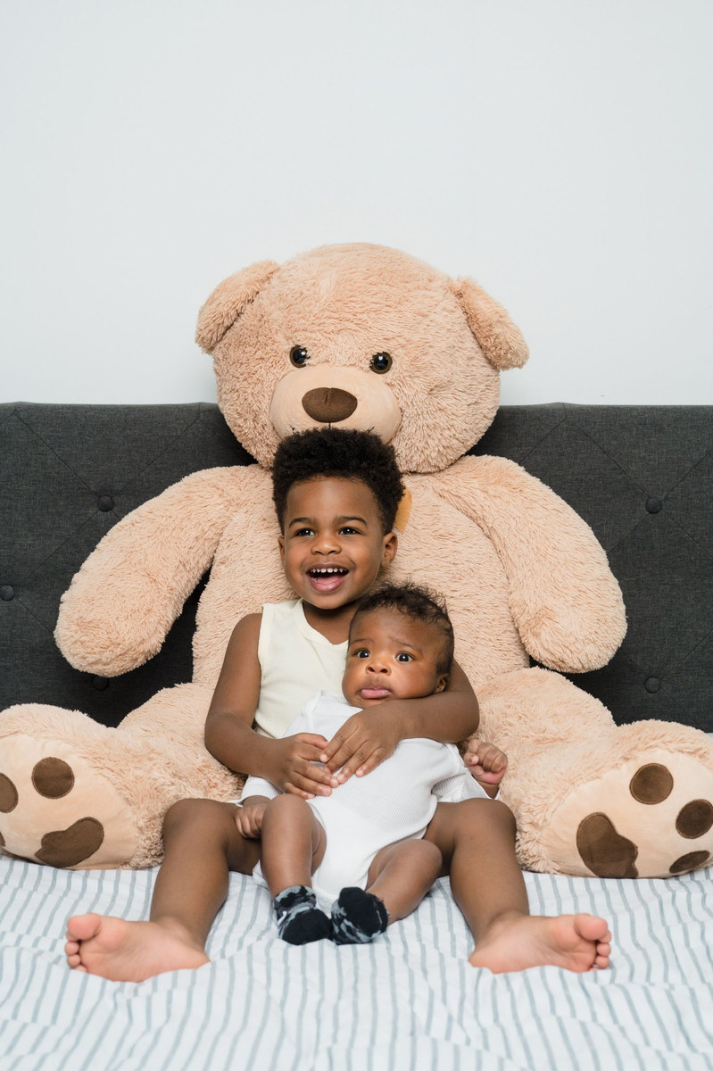 Young boy holding a baby in front of a large teddy bear