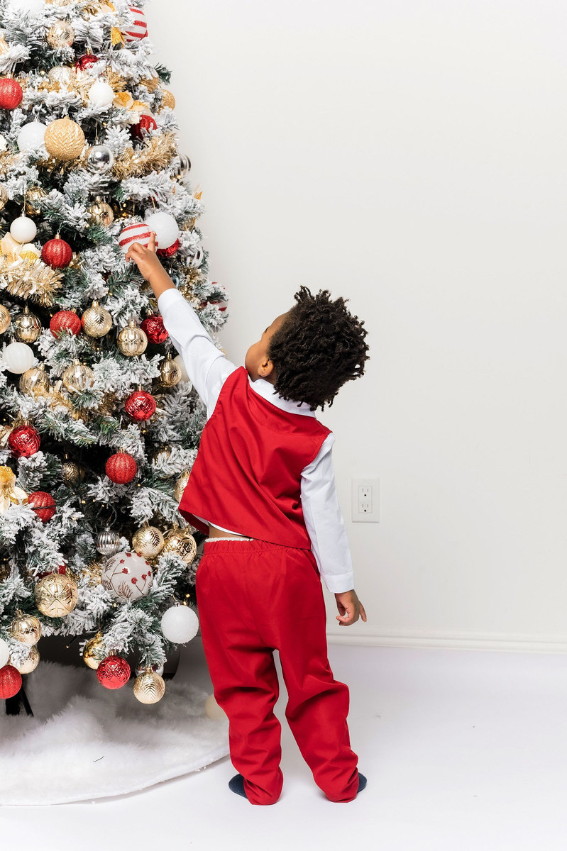 Toddler in a red outfit reaching up to touch a Christmas tree ornament