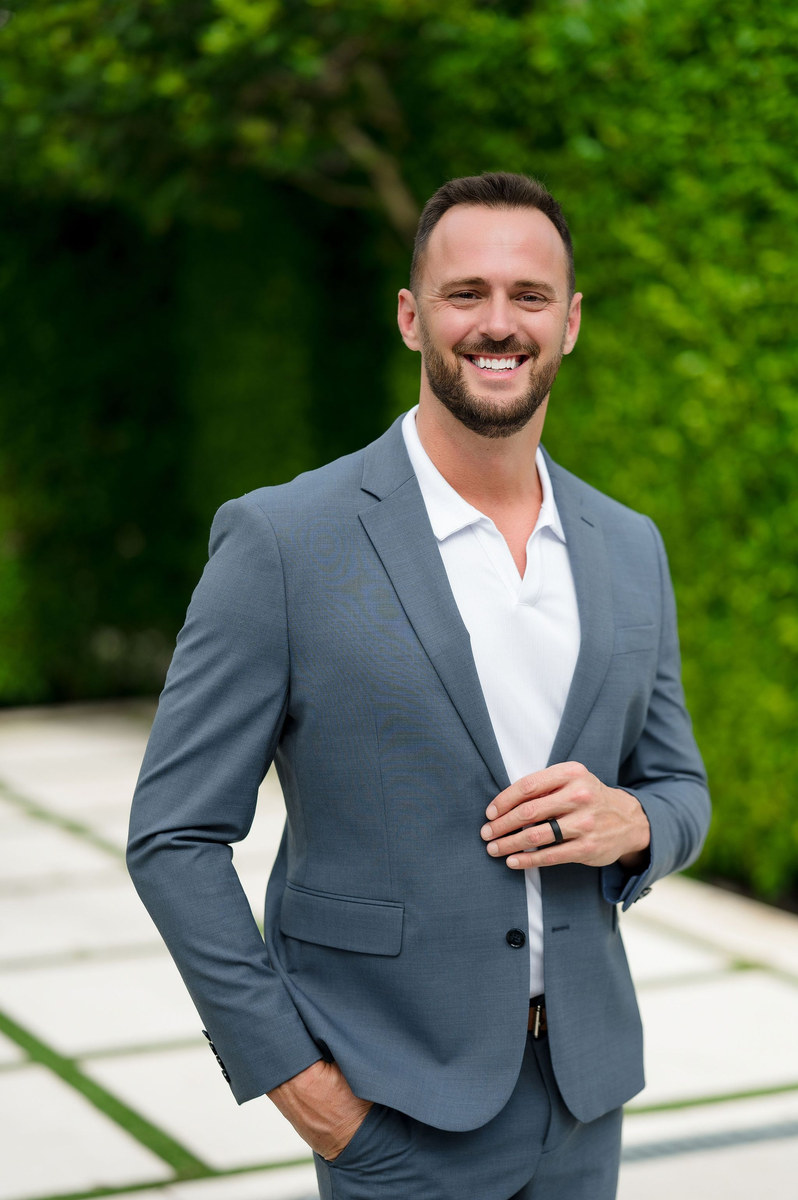 Man in a gray suit smiling on a garden walkway