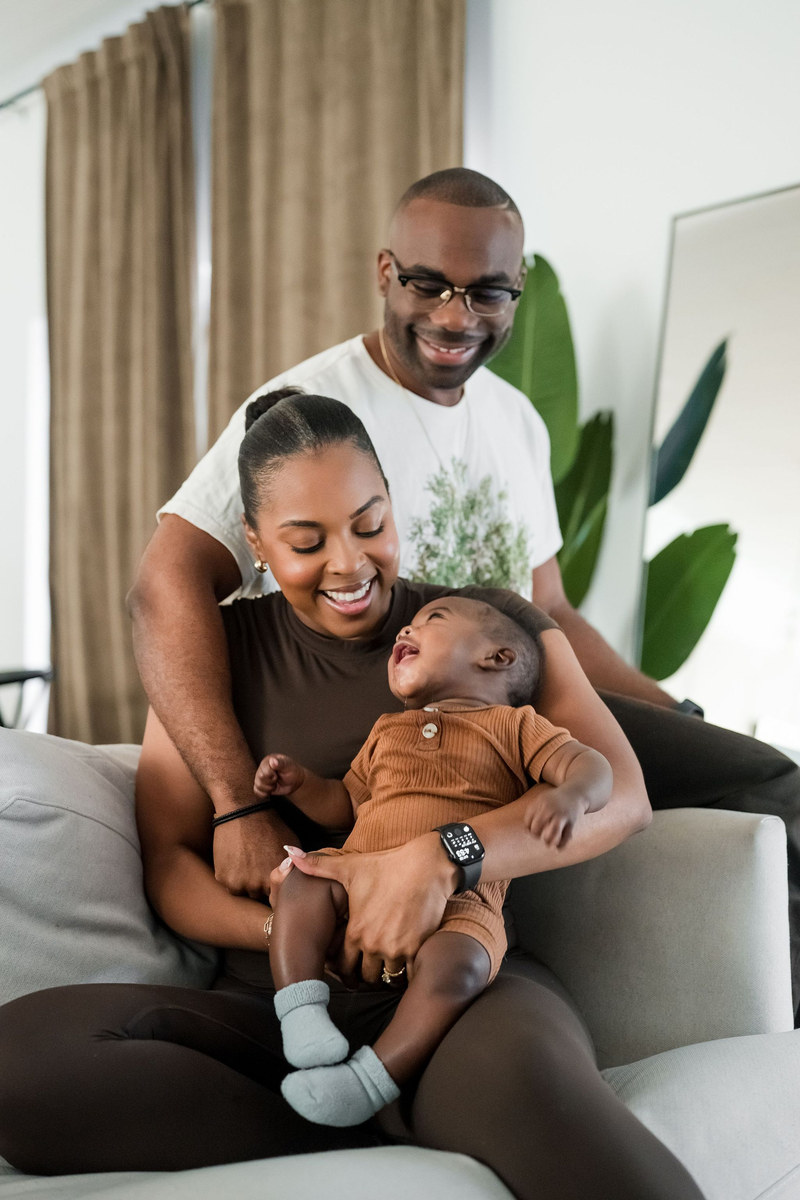 Parents laughing on a couch while holding their baby