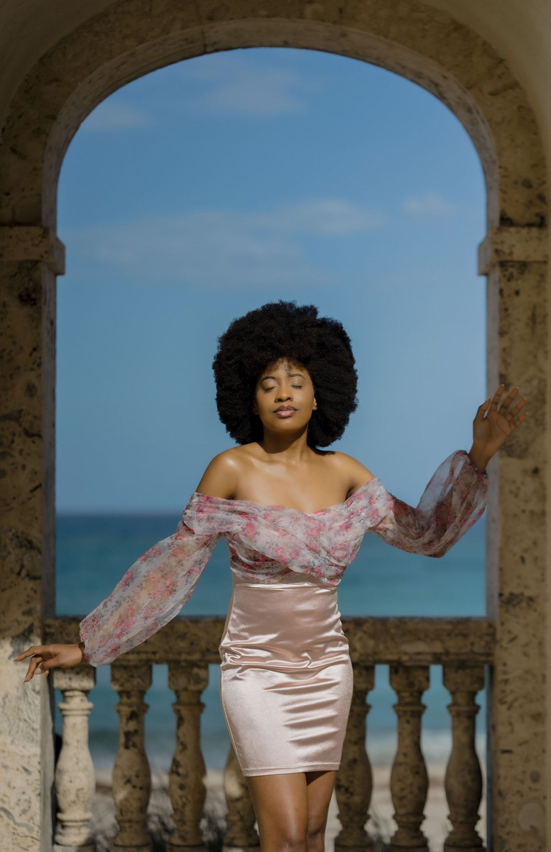 Woman in a pink off-the-shoulder dress posing in a stone archway above the ocean