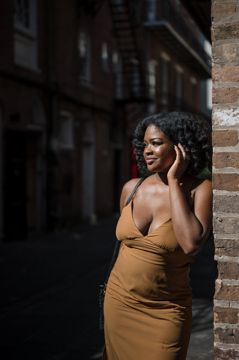 Woman in a tan slip dress leaning against a brick wall in evening light